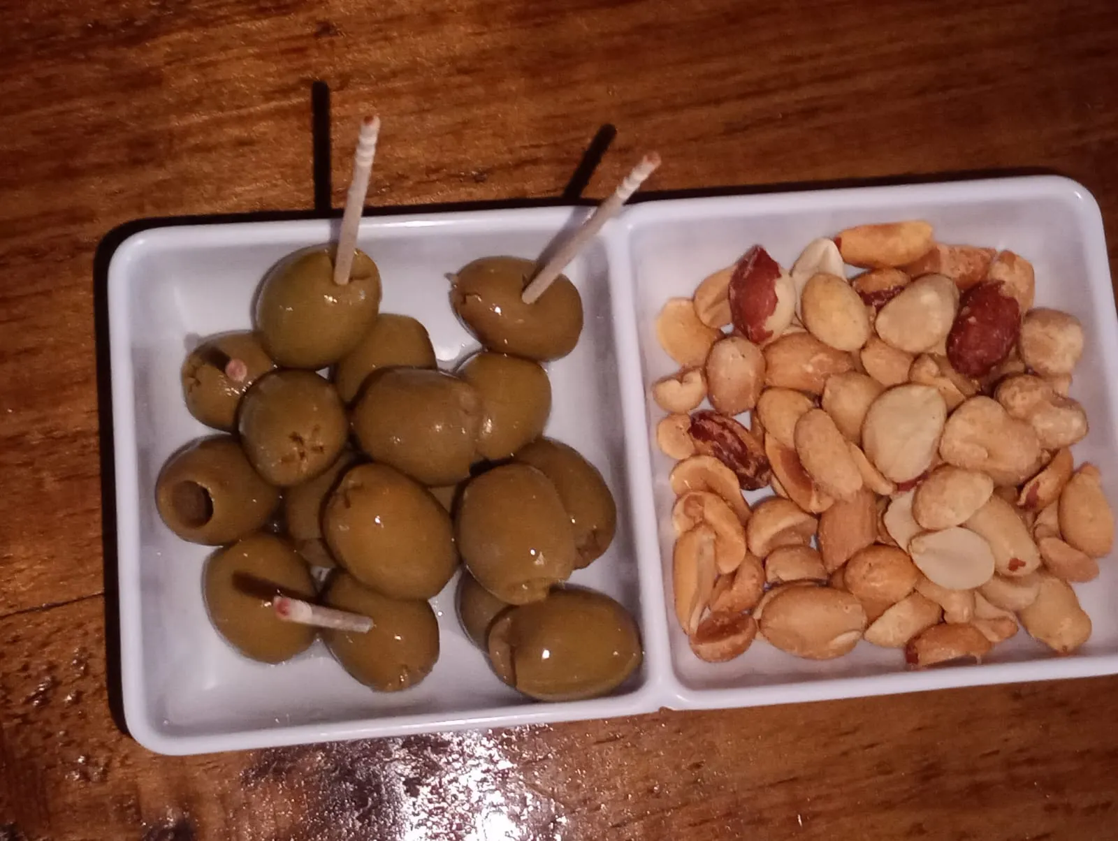 Olives and peanuts in two small white dishes on the bar