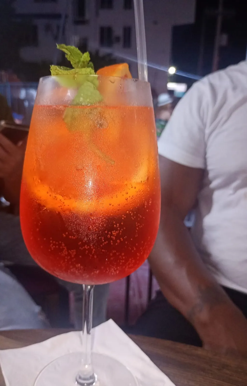 An Aperol spritz with mint and orange on a table at night